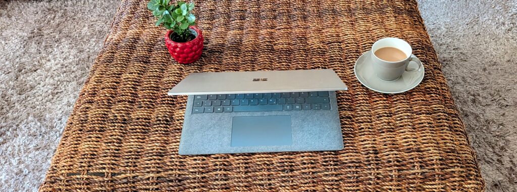 Laptop, Kaffeetasse und kleiner Blumenstock auf einem Rattan-Couchtisch - Symbolbild für Onlineberatung Symbolbild für Onlineberatung