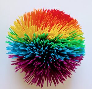 Bunter weicher Ball mit vielen elastischen Gummifäden auf einer hellen Oberfläche.